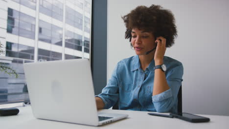 Young-Businesswoman-In-Modern-Office-Working-On-Laptop-Using-Wireless-Headset