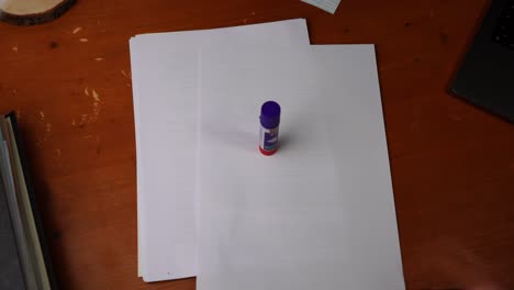 una pequeña barra de pegamento se coloca sobre un papel blanco sobre una mesa de madera y se retira