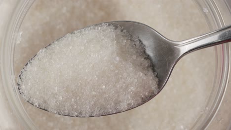cuchara tomando el azúcar granulado blanco del recipiente y luego vertiéndolo, disparado de arriba hacia abajo