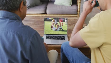 Video-Von-Verschiedenen-Männlichen-Freunden,-Die-Auf-Dem-Sofa-Sitzen-Und-Zu-Hause-Auf-Dem-Laptop-Fußball-Schauen