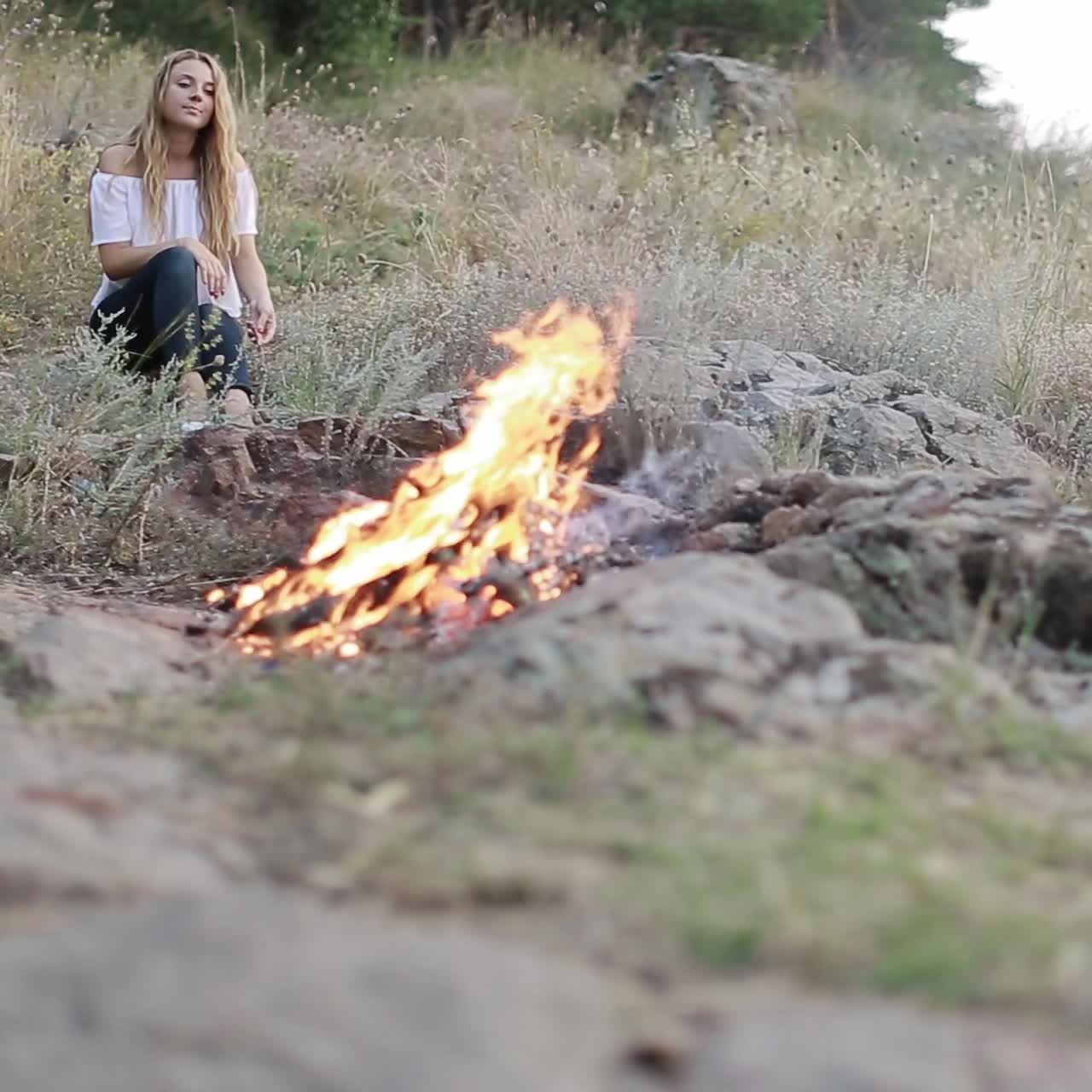 молодая женщина сидит возле костра