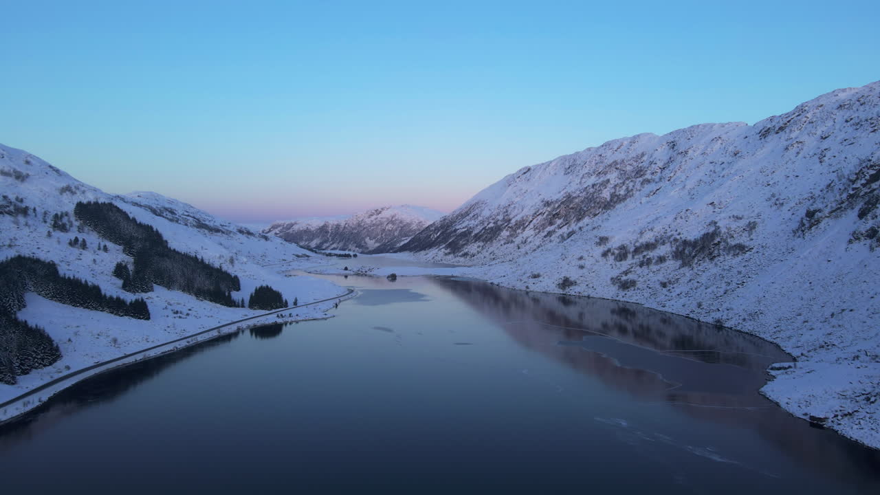 Droonikuva lumisesta Norjan vuoristomaisemasta, jossa järvi ja auringonlasku taustalla