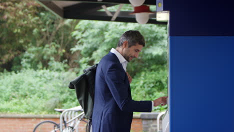 hombre de negocios que viaja haciendo pago sin contacto para el billete de tren en la máquina de la estación con tarjeta