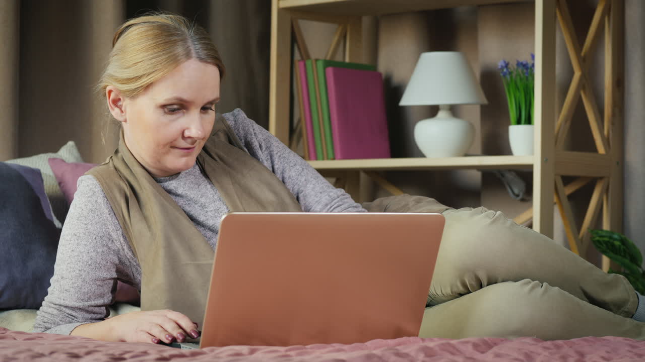 una mujer de mediana edad usa una computadora portátil en su cama