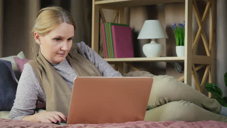 a middle-aged woman uses a laptop on her bed