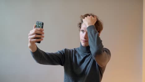 handsome young curly guy examines a hairstyle on a smartphone