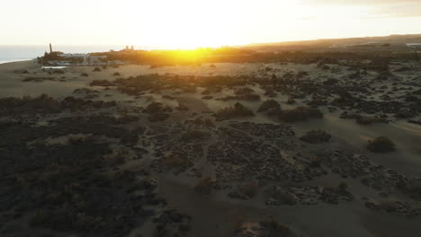 orbital aerial view of the maspalomas dunes during sunset and the beach lighthouse