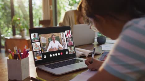 Schoolgirl-using-laptop-for-online-lesson-at-home,-with-diverse-teacher-and-class-on-screen