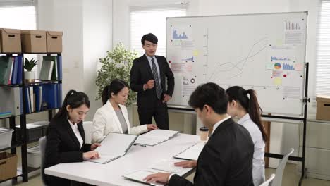 cheerful asian businessman talking giving briefing on new project in conference room at company. he gestures at the folder and tell colleagues to open and look at them