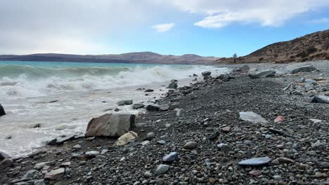 Rocky-shore-of-Lake-Pukaki,-NZ-on-a-windy-day