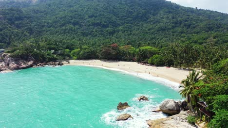 tranquila y exótica playa de arena blanca entre grandes acantilados, rodeada de palmeras y exuberante vegetación, bañada por una laguna color turquesa