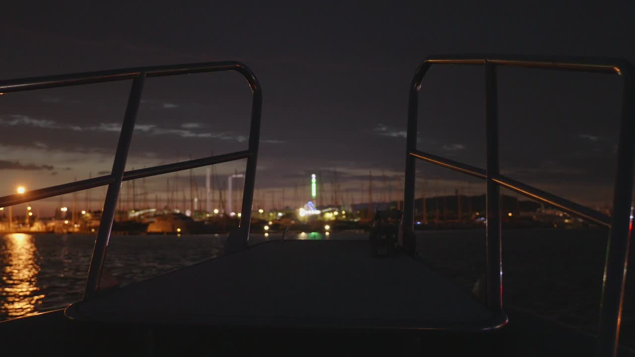 Bow Of A Speedboat Navigating At Night Over The Ocean Near A Coastal City. POV Shot