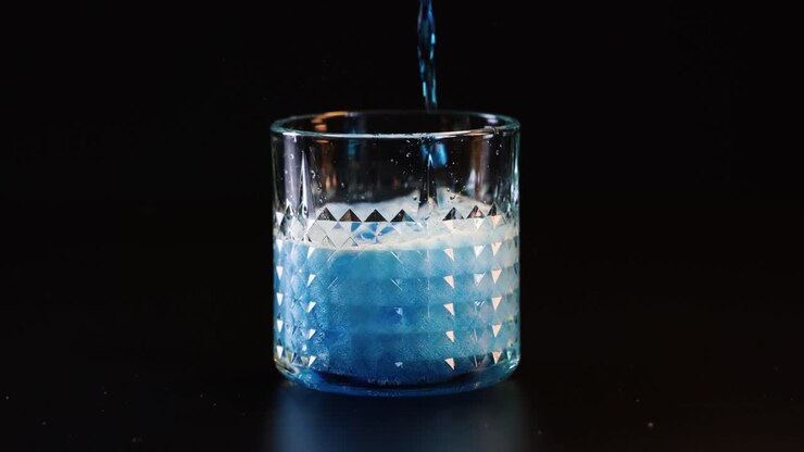 Liquido blu versato in un bicchiere, creando effervescenza
