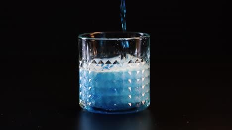 blue liquid poured into glass, creating fizz