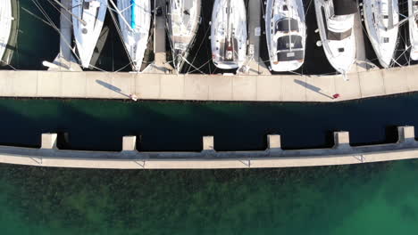 Luftaufnahme-Direkt-über-Luxuriösen-Segelyachten,-Die-In-Einem-Yachthafen-Auf-Türkisfarbenem-Wasser-Festgemacht-Sind