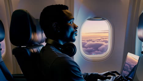 man working on laptop during an airplane flight with scenic cloud view