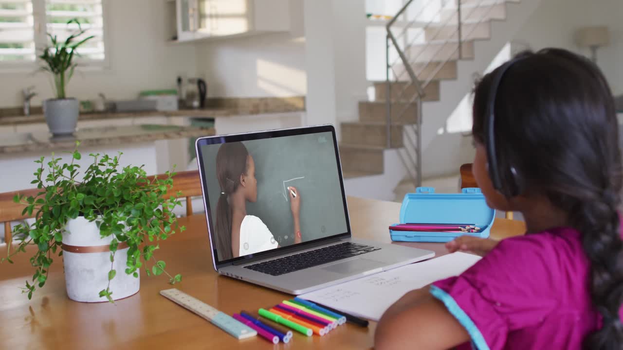 Niña mestiza sentada en el escritorio usando una computadora portátil tomando una clase escolar en línea