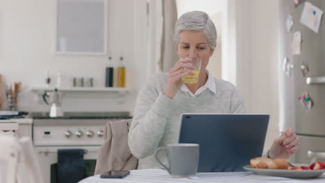 happy mature woman using laptop computer at home drinking juice typing messages browsing online enjoying working in morning at breakfast 4k footage