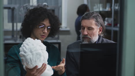 two men discussing a sculpture in an art studio