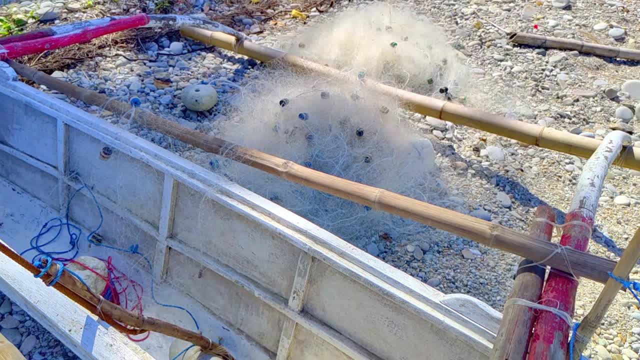 Fishing nets draped over a wooden banca under dappled sunlight on a tropical beach in the Philippines.