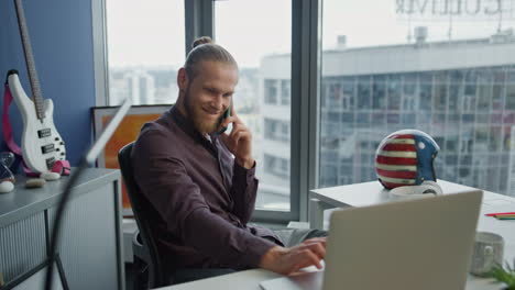 Trabajador-Independiente-Alegre-Llamando-Al-Móvil-En-El-Primer-Plano-De-La-Oficina-En-Casa.-Hombre-Mirando-Computadora