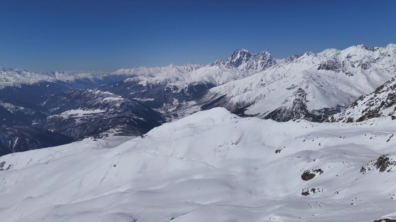 Una veduta aerea laterale da drone mostra le vaste montagne del Caucaso coperte di neve sotto un cielo blu cristallino, rivelando infinite creste alpine e una natura selvaggia invernale incontaminata vicino a Mestia, Georgia.