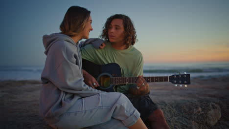una pareja sonriente toca la música de la guitarra en la playa al atardecer. una mujer relajada cantando una canción.
