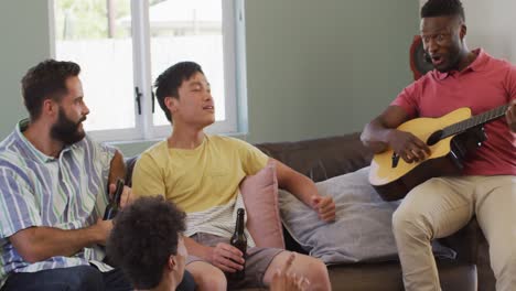 Happy-diverse-male-friends-playing-guitar-and-talking-in-living-room