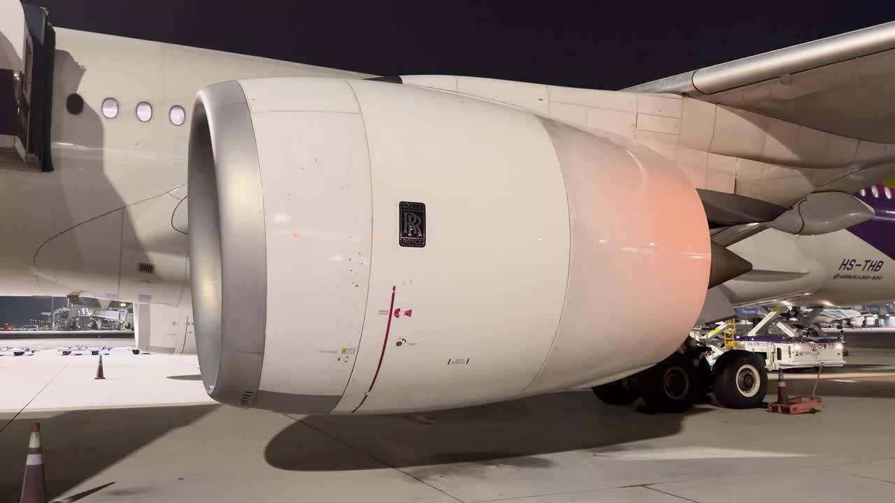 Primo piano di un motore di un aereo commerciale bianco parcheggiato sul piazzale di un aeroporto di notte