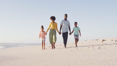 Smiling-african-american-holding-hands-and-walking-on-sunny-beach