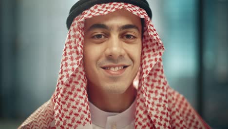 portret młodego, odnoszącego sukcesy arabskiego biznesmena w tradycyjnym stroju, delikatnie uśmiechającego się, noszącego białą kandurę i czarny agal, trzymającego ghutrę na miejscu.