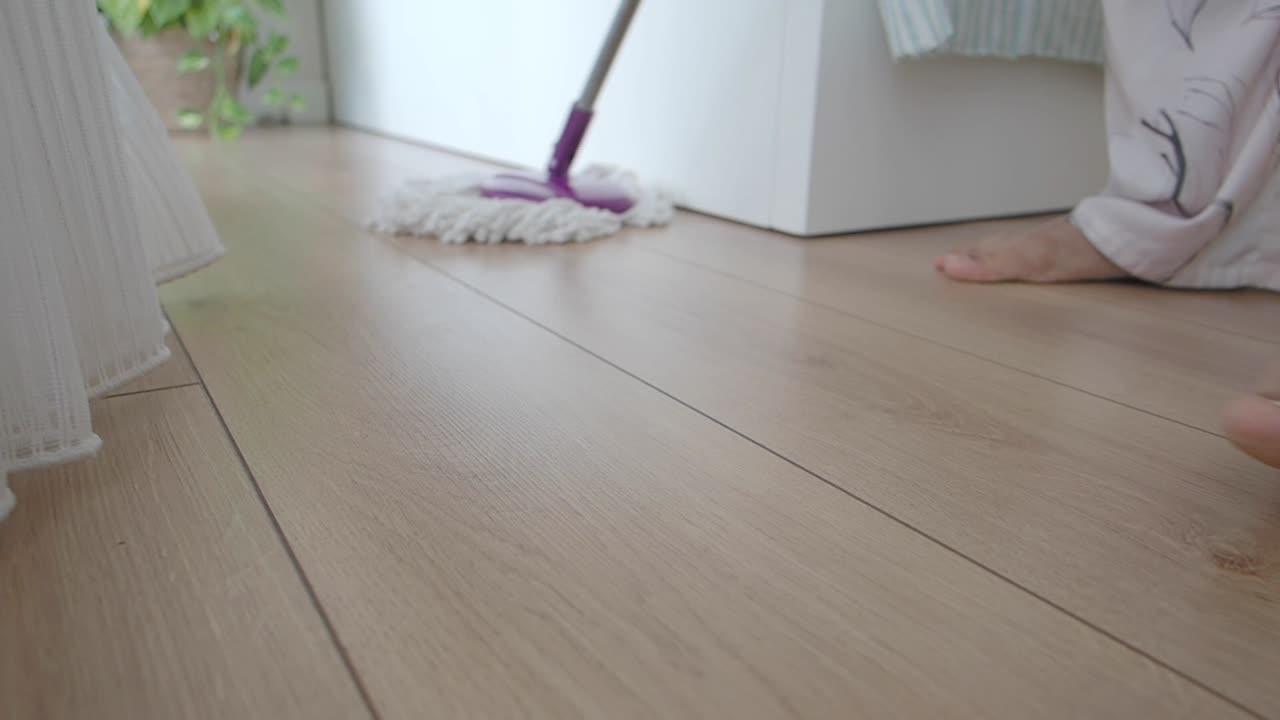 Person mopper tregulv i klær hjemme