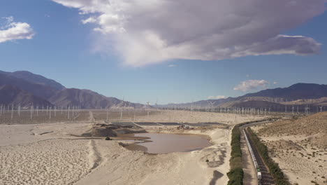 Antena-De-Un-Tren-De-Carga-Que-Pasa-Cerca-Del-Parque-Eólico-De-Palm-Springs,-Montañas-A-Lo-Lejos