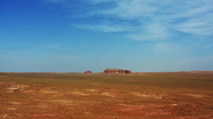 A gorgeous desert view of a large white and red butte rock formation isolated in the middle of the Utah desert near the Goblin Valley State Park on a warm summer day