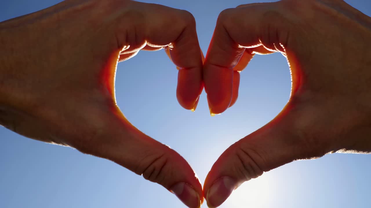 Hands form a heart shape against a bright sky, captured from a low angle