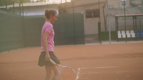 A-tired-brunette-female-tennis-player-walks-along-the-tennis-court-recuperating-and-concentrating.-Break-in-a-tennis-match.-Tennis-player-after-the-match-on-the-map-at-sunset-in-slow-motion.