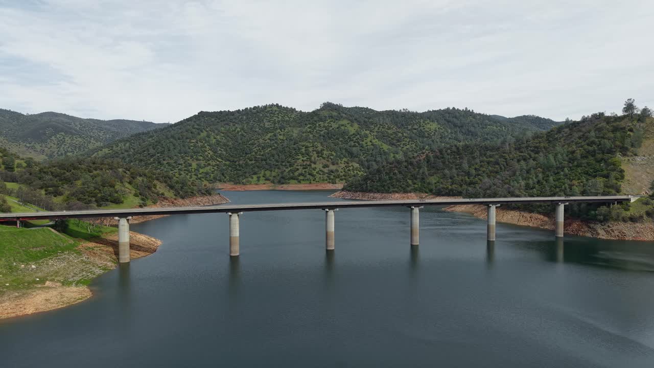 Drone captures cars smoothly passing over the Don Pedro Reservoir Bridge, with the landscape extending to the horizon.