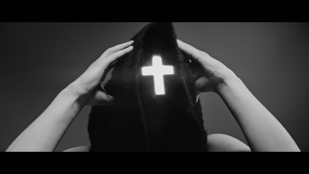 Masked man with cross of light glowing on his face grabs his head with his hand