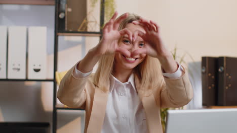 young business woman makes symbol of love, showing heart sign to camera, express romantic feelings