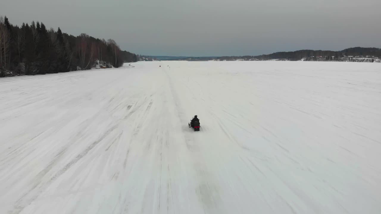 Tracking aerial shot of a man driving his snowmobile on Indalsalven in Timra, Sundsvall, Sweden.