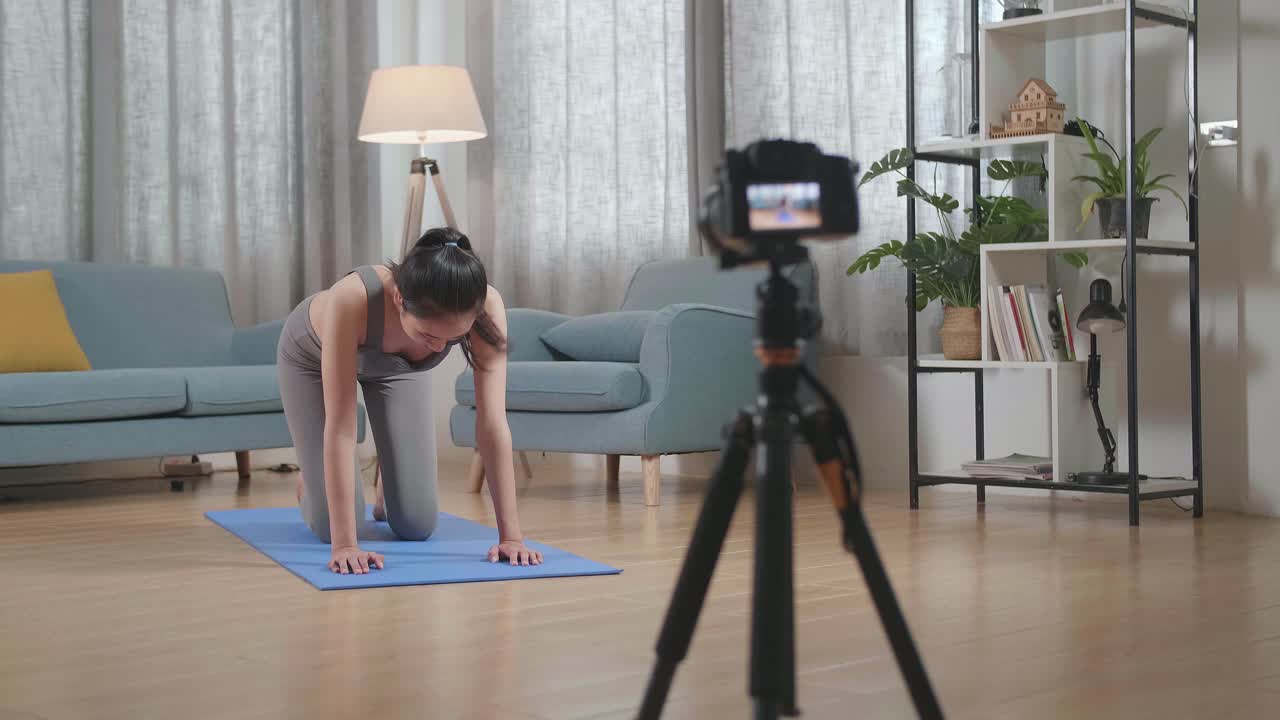 vista completa de joven entrenadora asiática mujer en ropa deportiva hablando a la cámara y haciendo yoga en postura de mesa de equilibrio mientras graba ejercicio de enseñanza en casa
