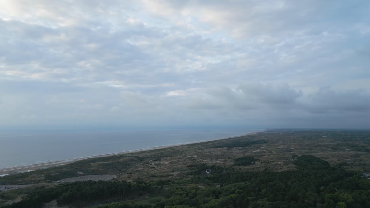 Peaceful drone view flying above the North Sea coast of the Netherlands, showing sand dunes, water inlets, and the horizon at sunset