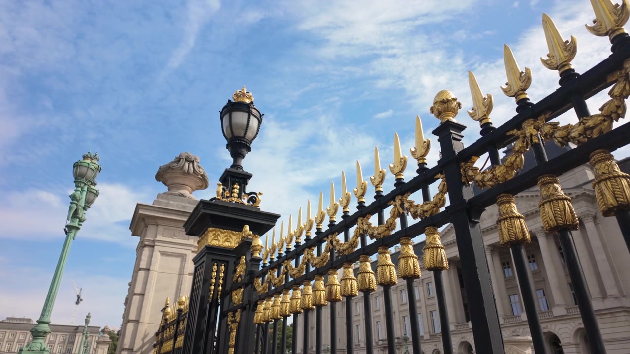 Cancelli ornati neri e dorati fuori dal palazzo reale a Bruxelles, con lampade decorative, colonne di pietra e un cielo nuvoloso di un blu brillante. Panoramica a destra.