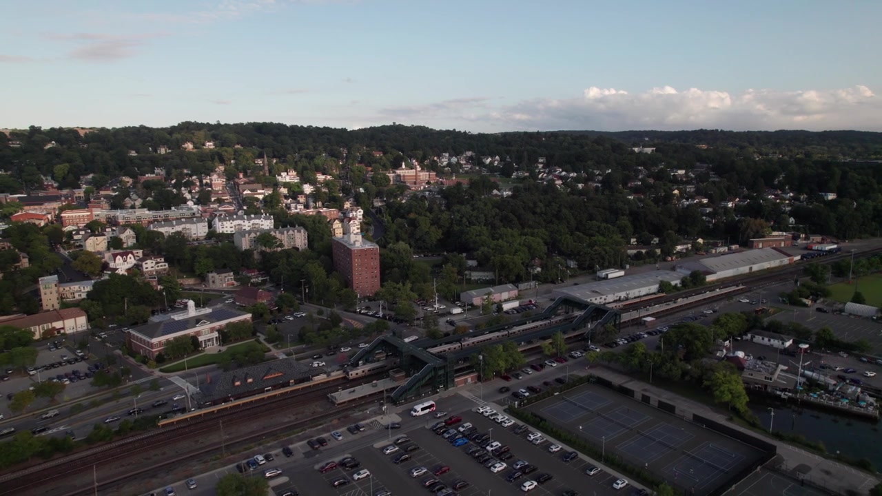 Toma aérea prolongada siguiendo el tren Metro North Railroad mientras entra en la estación de Tarrytown, Estado de Nueva York