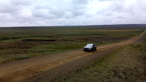 aerial circular shot of a car passing by on a lonely gravel mountain road in iceland