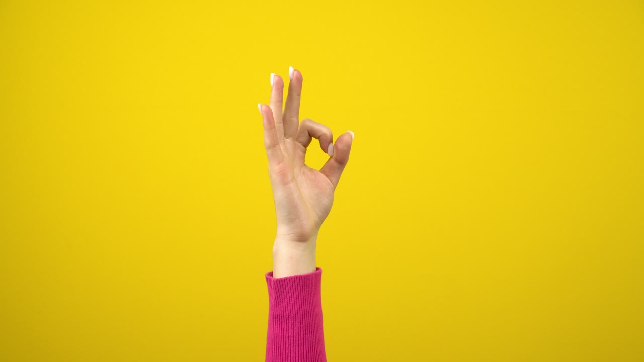 женская рука показывает знак ok. студийная фотография на изолированном желтом фоне.