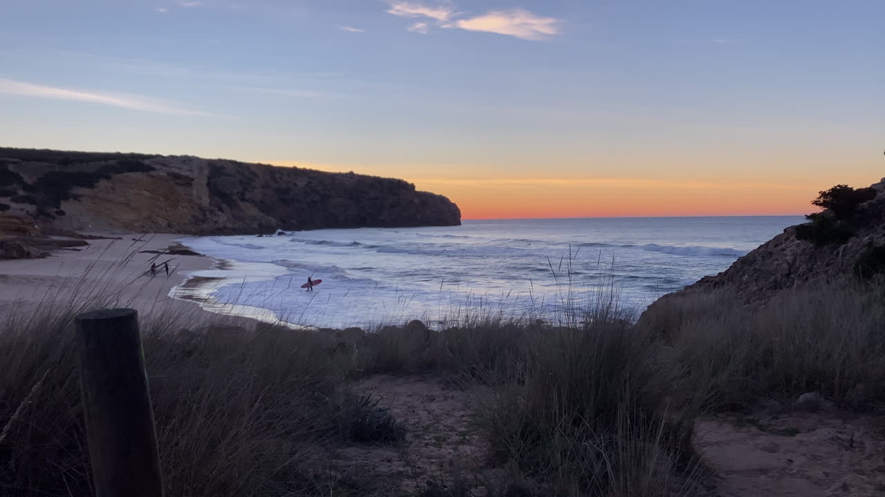 Surfisti che camminano nell'Oceano Atlantico con le tavole da surf su una spiaggia sabbiosa, godendosi lo stile di vita costiero al tramonto in Portogallo