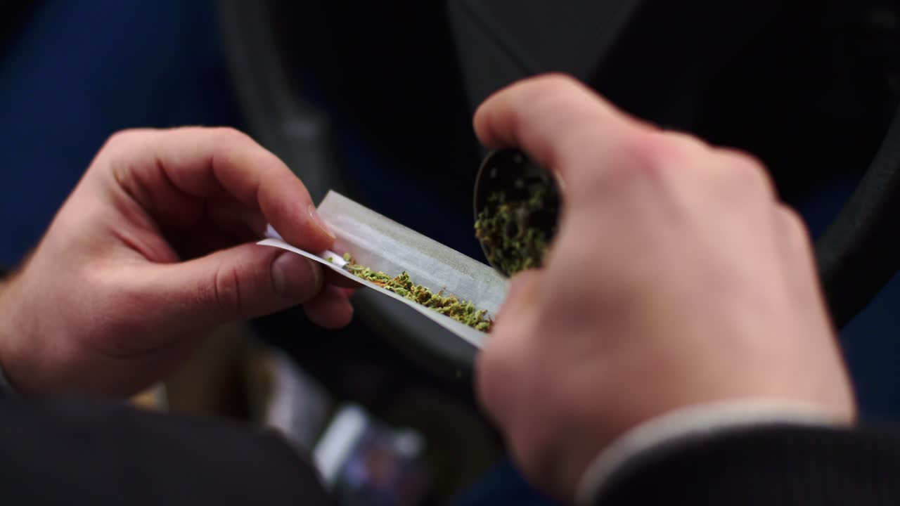 Close-up of hands using grinder to break down cannabis, rolling a joint in car