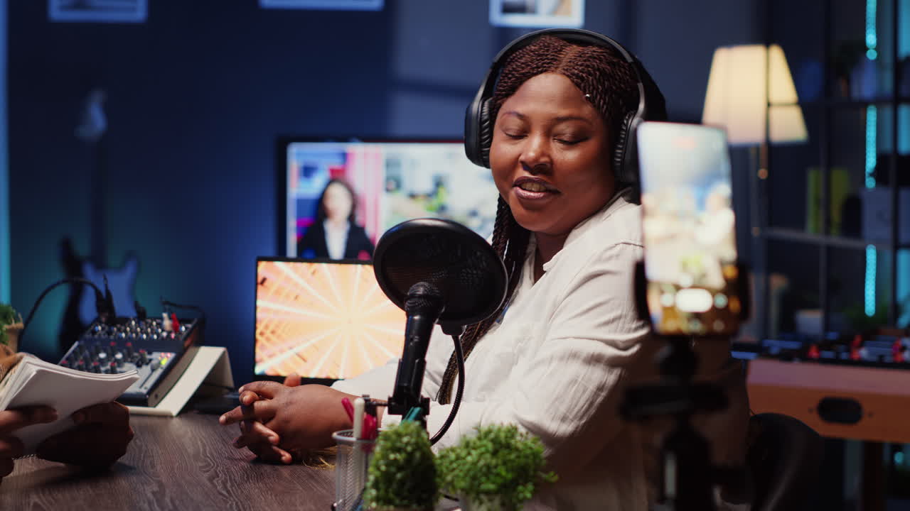 기자가 휴대전화로 인터뷰를 녹음하고, 스튜디오에서 삼각대 안정화 장치에 탑재하여 메모를 검토합니다.