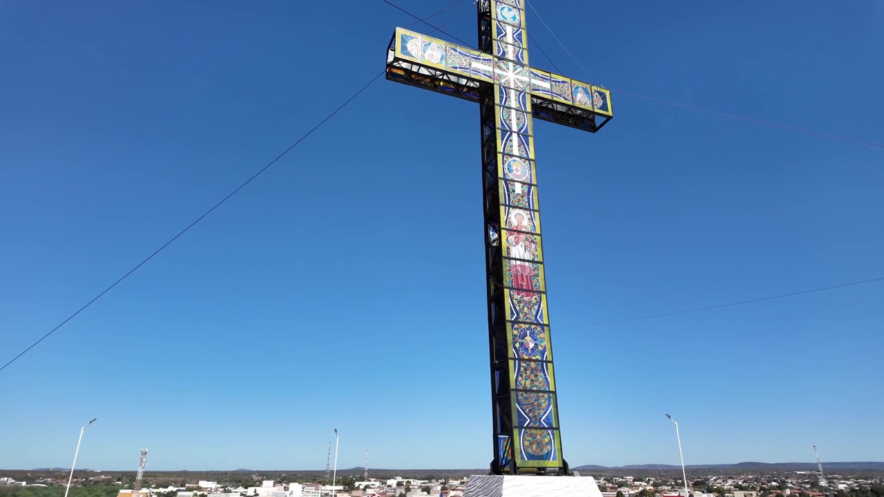 Korkea ja värikäs mosaiikkiristimonumentti seisoo katolla sijaitsevalla näköalapaikalla Sao Raimundo Nonaton kaupungin yläpuolella kirkkaan sinisen taivaan alla